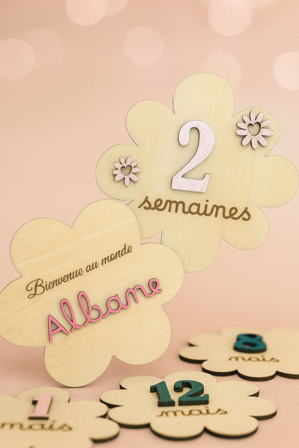 2 cartes en bois en forme de fleur : l'une gravée "Bienvenue au monde" avec le prénom "Albane" peint en rose et collé puis l'autre avec le numéro "2" peint en rose pâle et collé avec 2 fleurs de la même couleurs et "semaines" gravé. Posées en dessous : 3 cartes étapes, 2 vertes et 1 rose pâle; Le fond de la poto est rose pâle