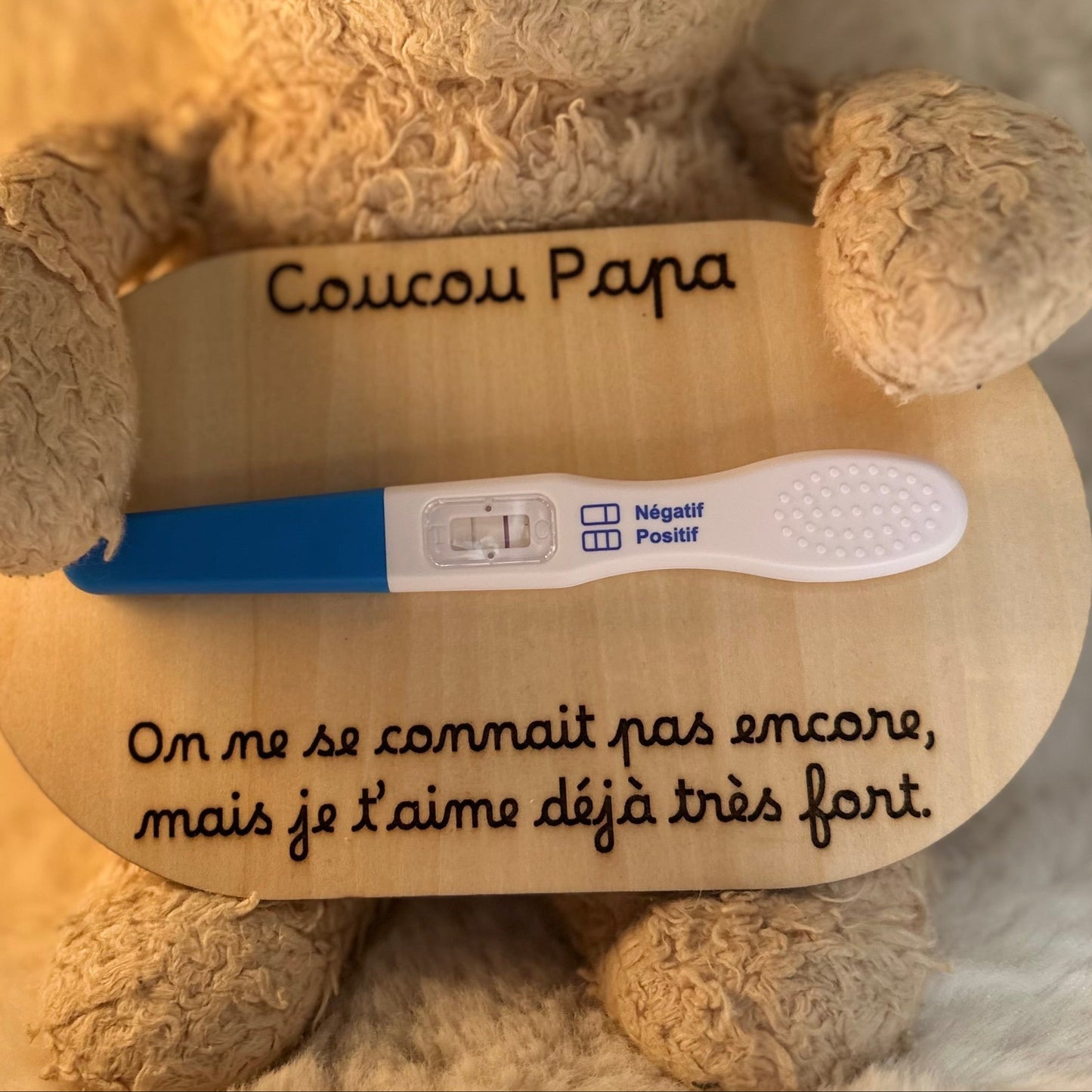 peluche tenant une carte en bois "coucou papa, on ne se connait pas encore, mais je t'aime déjà très fort" et un test de grossesse positif