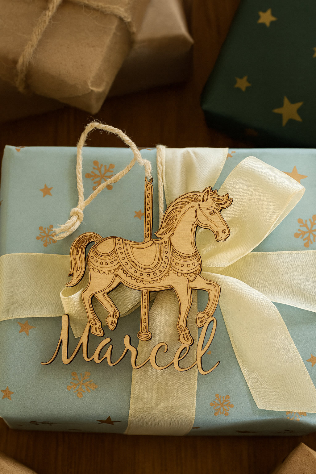 cheval de carrousel en bois personnalisé avec prénom de l'enfant "marcel" et posé sur un cadeau bleu cel avec des étoiles et un ruban blanc