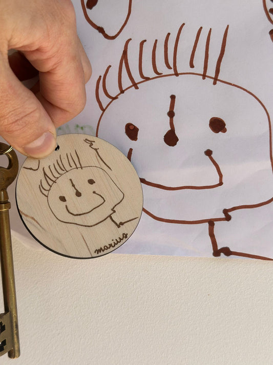 dessin d'un bonhomme réalisé par un jeune enfant et la reproduction gravée sur un porte clef en bois