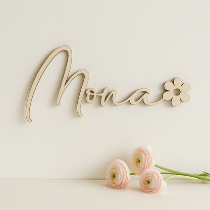 prénom en bois : Mona se terminant par une fleur et fixé sur un mur blanc cassé, en dessous une commode sur laquelle sont posées 3 renoncules blanche et rosées
