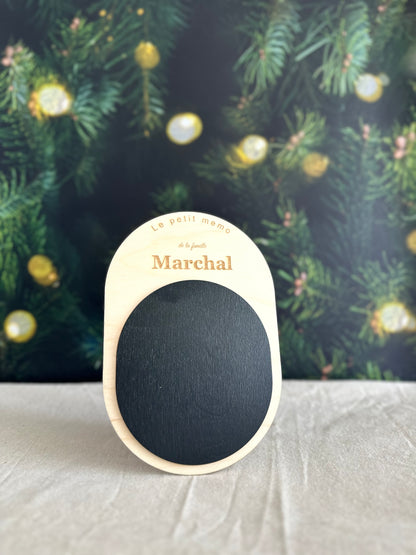 Cadeau de Noël personnalisé pour la famille : ardoise mémo aimantée en bois gravée « Le petit mémo de la famille Marchal », posée devant un sapin illuminé