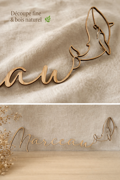 détails du prénom en bois et de l baleine finement découpée au laser, le prénom, en bas, "Marceau" est posé contre un linge en lin sur une commode. En haut l'infographie "découpe fine et bois naturel"