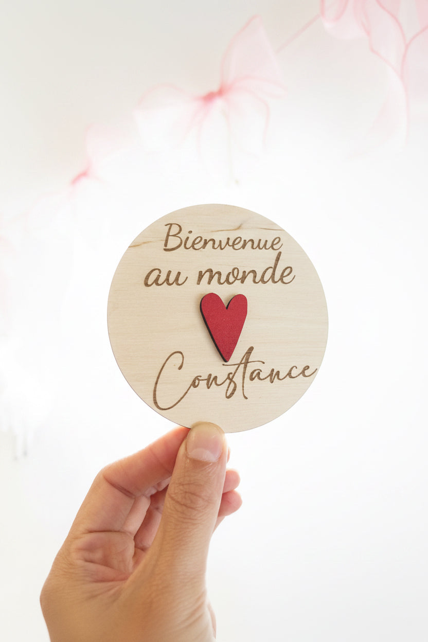 carte en bois ronde annonce naissance personnalisée avec le prénom de bébé et un coeur rouge fixé au milieu "bienvenue au monde Constance"
