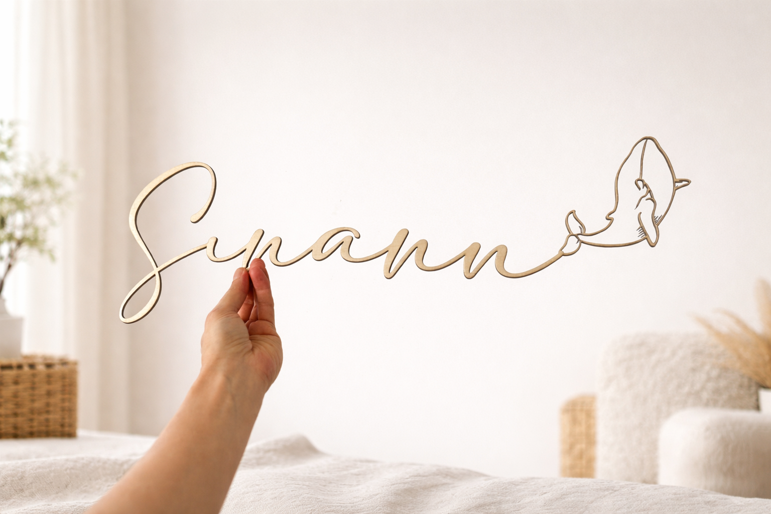 prénom en bois se terminant par une baleine finement découpé au laser pour décoré une chambre. Le prénom en bois "Sinann" est tenu par une main dans une chambre élégante. 