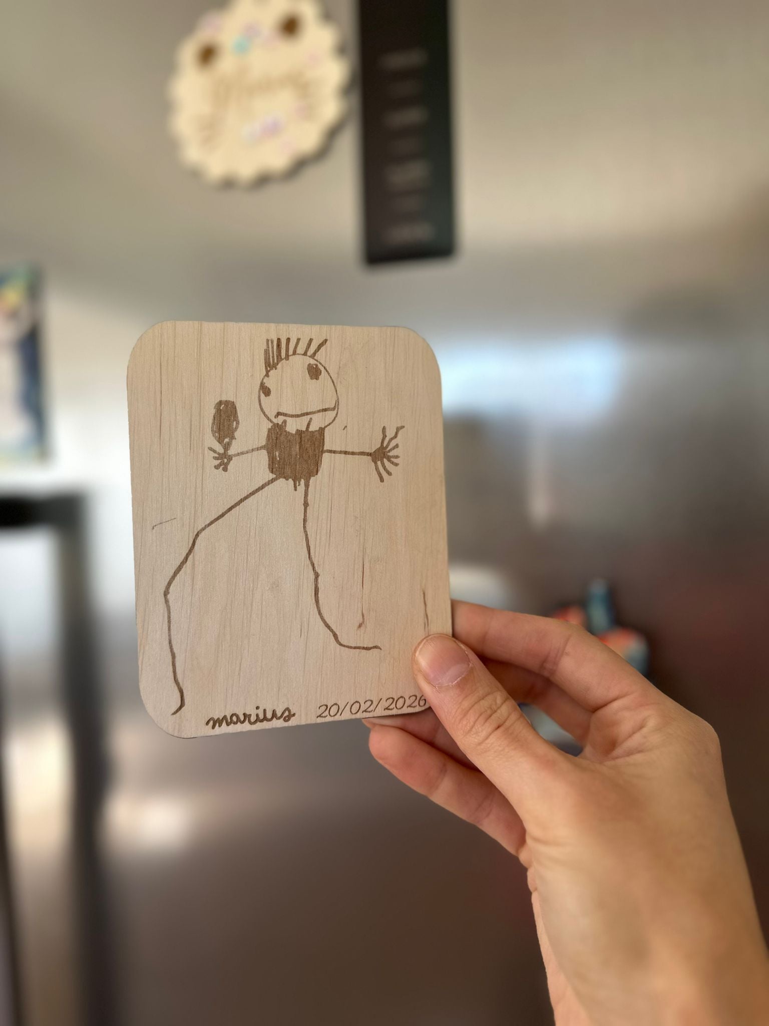 une main tient le dessin de votre enfant reproduit sur une carte en bois