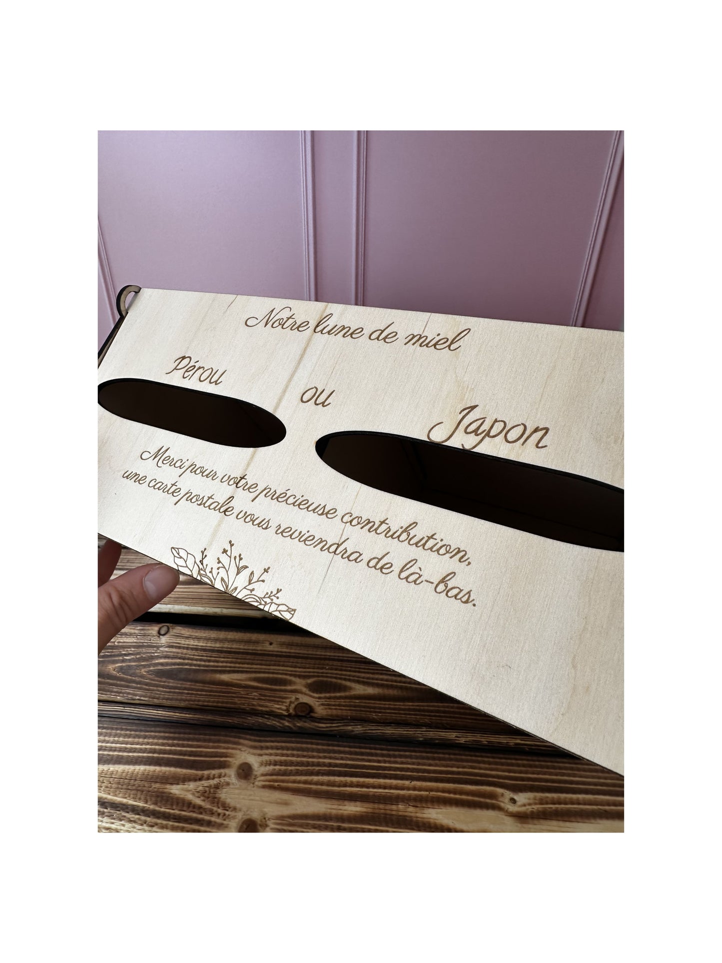 vue du dessus de l'Urne mariage en bois personnalisée "notre lune de miel" et message gravé personnalisé "Pérou ou Japon Merci pour votre précieuse contribution, une carte postale vous reviendra de là-bas" .IL y a 2 entrées pour voter pour destination lune de miel. le fond est rose et la table sur laquelle est posée l'urne est en bois massif 