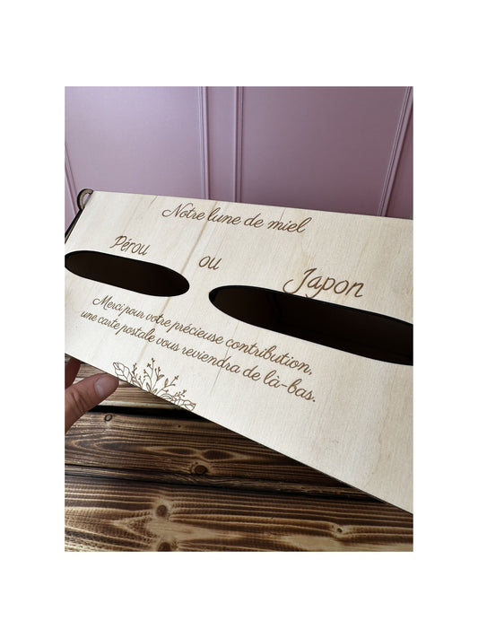 vue du dessus de l'Urne mariage en bois personnalisée "notre lune de miel" et message gravé personnalisé "Pérou ou Japon Merci pour votre précieuse contribution, une carte postale vous reviendra de là-bas" .IL y a 2 entrées pour voter pour destination lune de miel. le fond est rose et la table sur laquelle est posée l'urne est en bois massif 