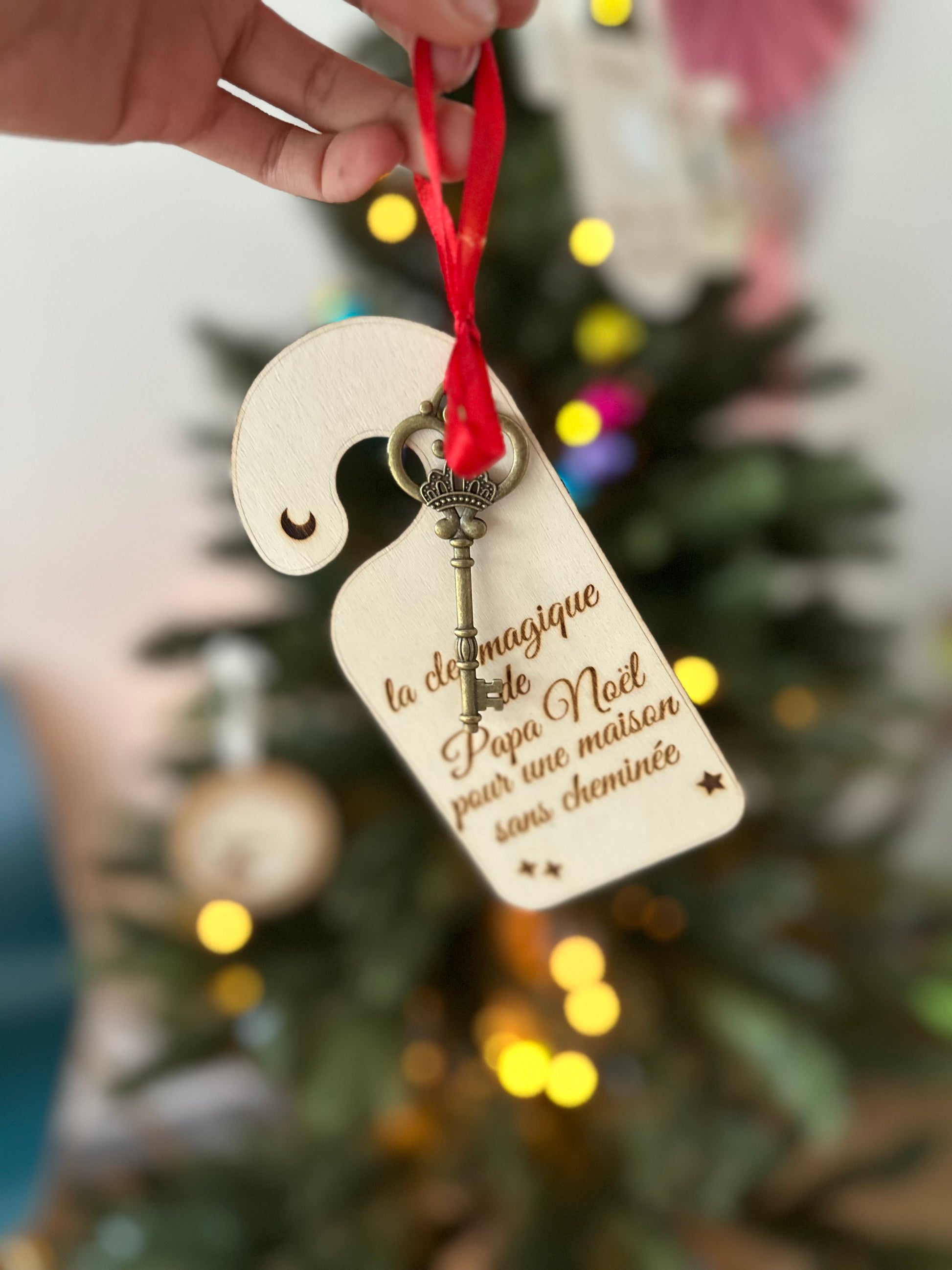 Clé magique de Papa Noël en bois, suspendue par un ruban rouge devant un sapin lumineux, avec petite clé dorée, pour les maisons sans cheminée.