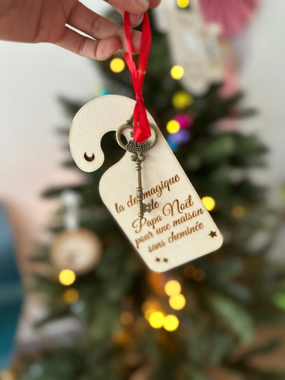 Clé magique de Papa Noël en bois, suspendue par un ruban rouge devant un sapin lumineux, avec petite clé dorée, pour les maisons sans cheminée.