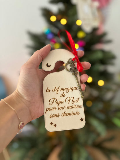 Clé magique de Papa Noël en bois, tenue en main devant un sapin de Noël illuminé, avec ruban rouge et clé dorée, pour les maisons sans cheminée.
