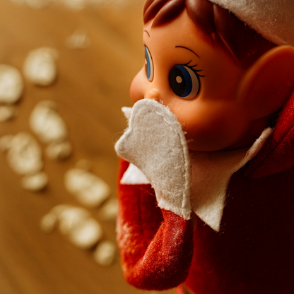 Gros plan sur un lutin farceur de Noël, les mains sur la bouche, devant des traces de pas en farine.