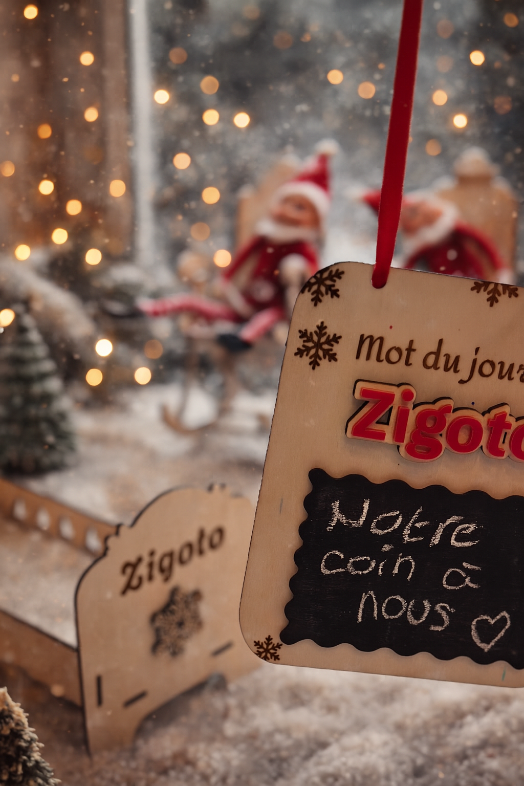 Lutin farceur assis dans un rocking chair en bois clair, les jambes rayées rouge et blanc allongées, au pied d’un sapin décoré de boules multicolores. La scène est lumineuse et festive, ambiance cosy de Noël