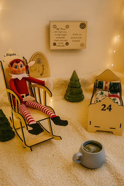 Lutin farceur installé dans un rocking chair en bois gravé “Zigoto”, devant une petite porte magique et un panneau miniature. À côté, un lit de lutin en bois et une tasse de tisane complètent la scène féérique sur une couverture en sherpa