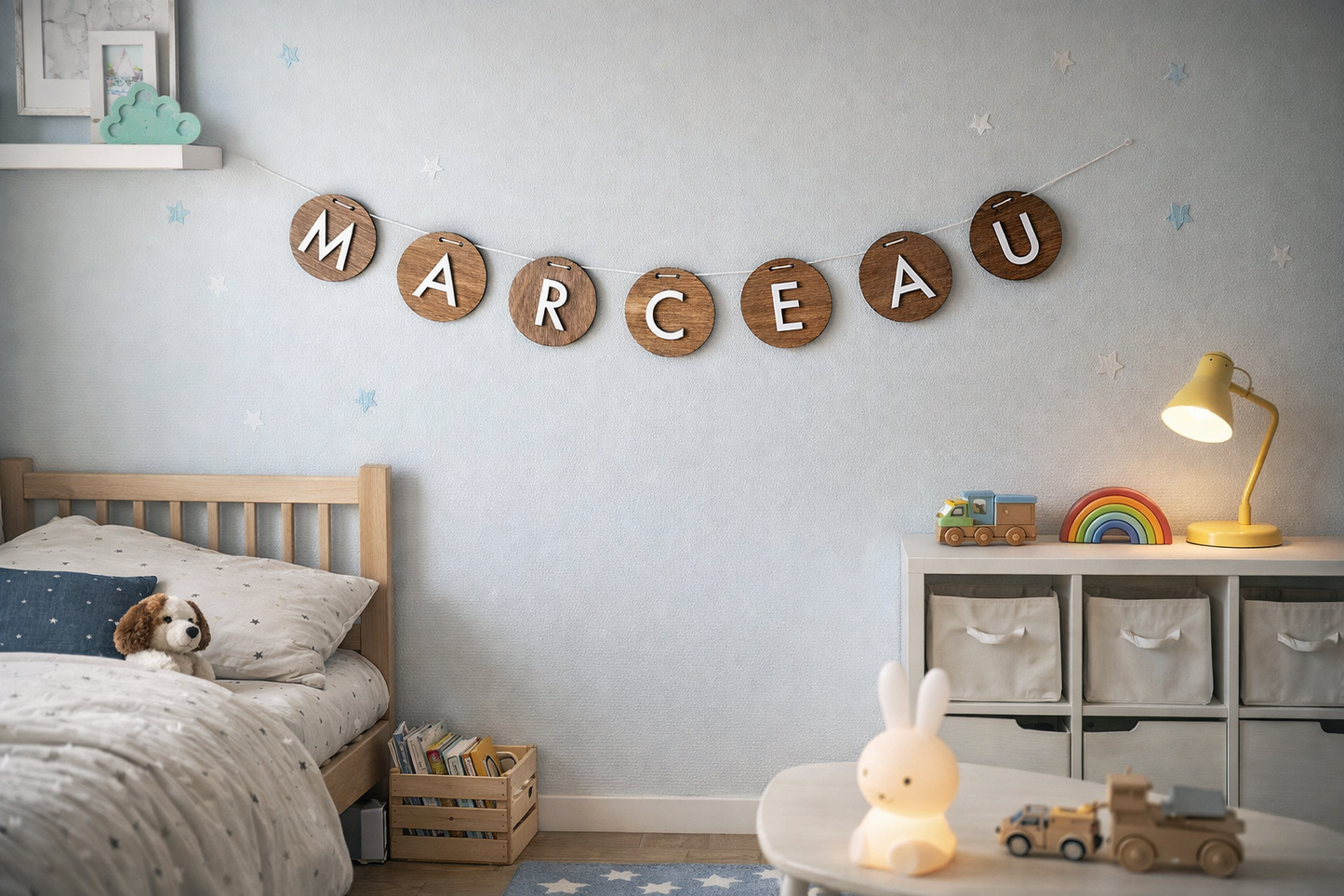 Guirlande prénom en bois composée de disques ronds suspendus par une ficelle, lettres blanches formant le prénom Marceau, posée sur un sol imitation parquet bois clair.