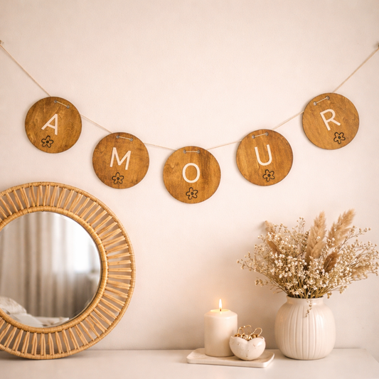 Guirlande murale en bois personnalisée “AMOUR” composée de disques ronds suspendus sur un mur clair, mise en scène au-dessus d’un miroir en rotin avec décoration naturelle et ambiance chaleureuse.