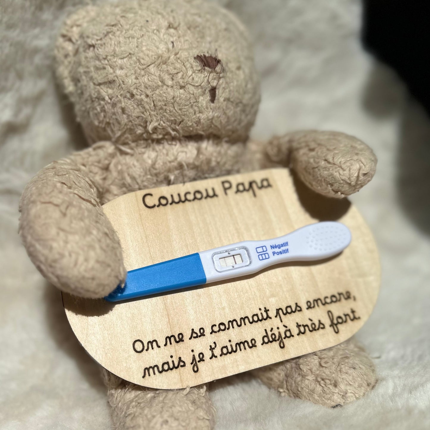 peluche tenant une carte en bois "coucou papa, on ne se connait pas encore, mais je t'aime déjà très fort" et un test de grossesse postitif