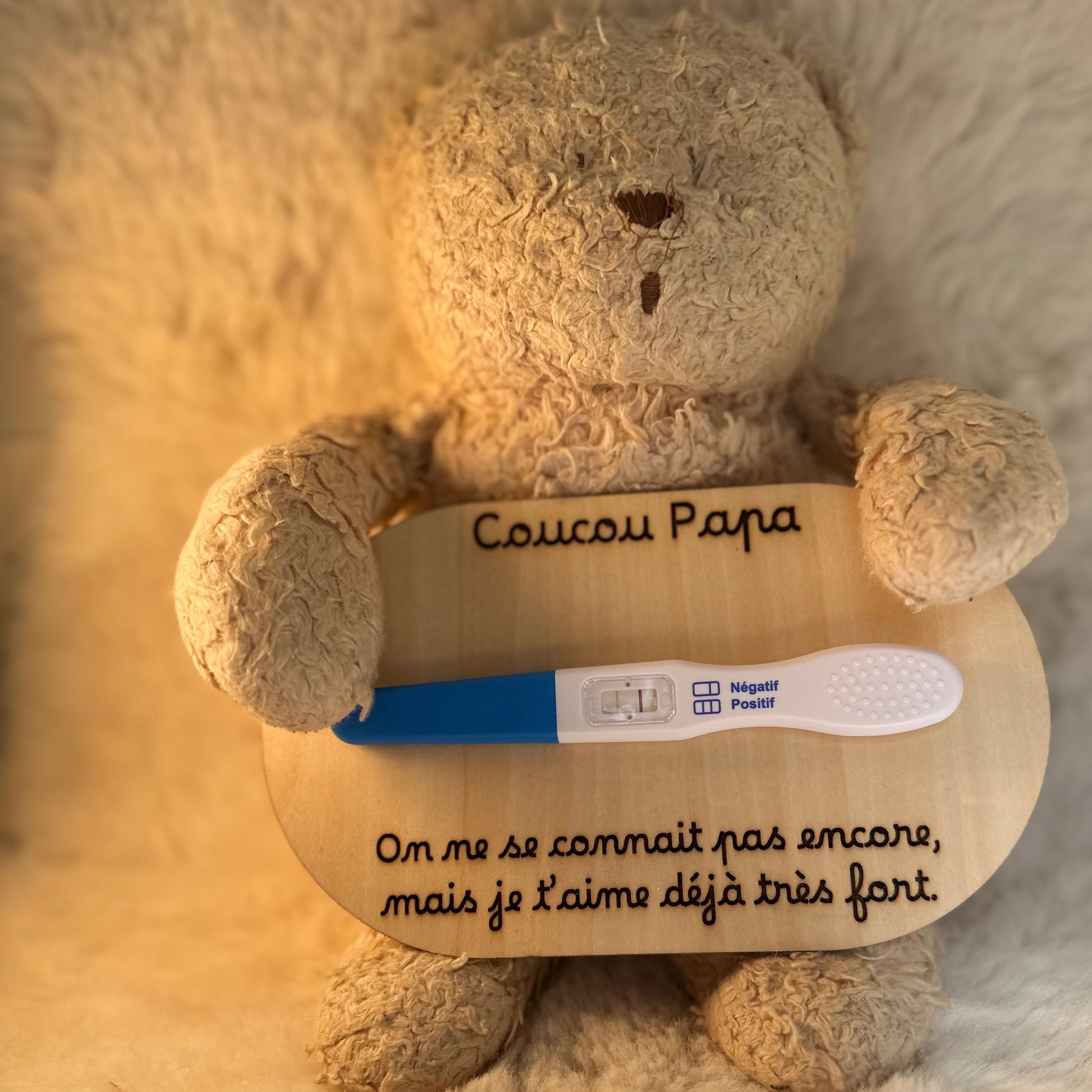 peluche tenant une carte en bois "coucou papa, on ne se connait pas encore, mais je t'aime déjà très fort" et un test de grossesse positif