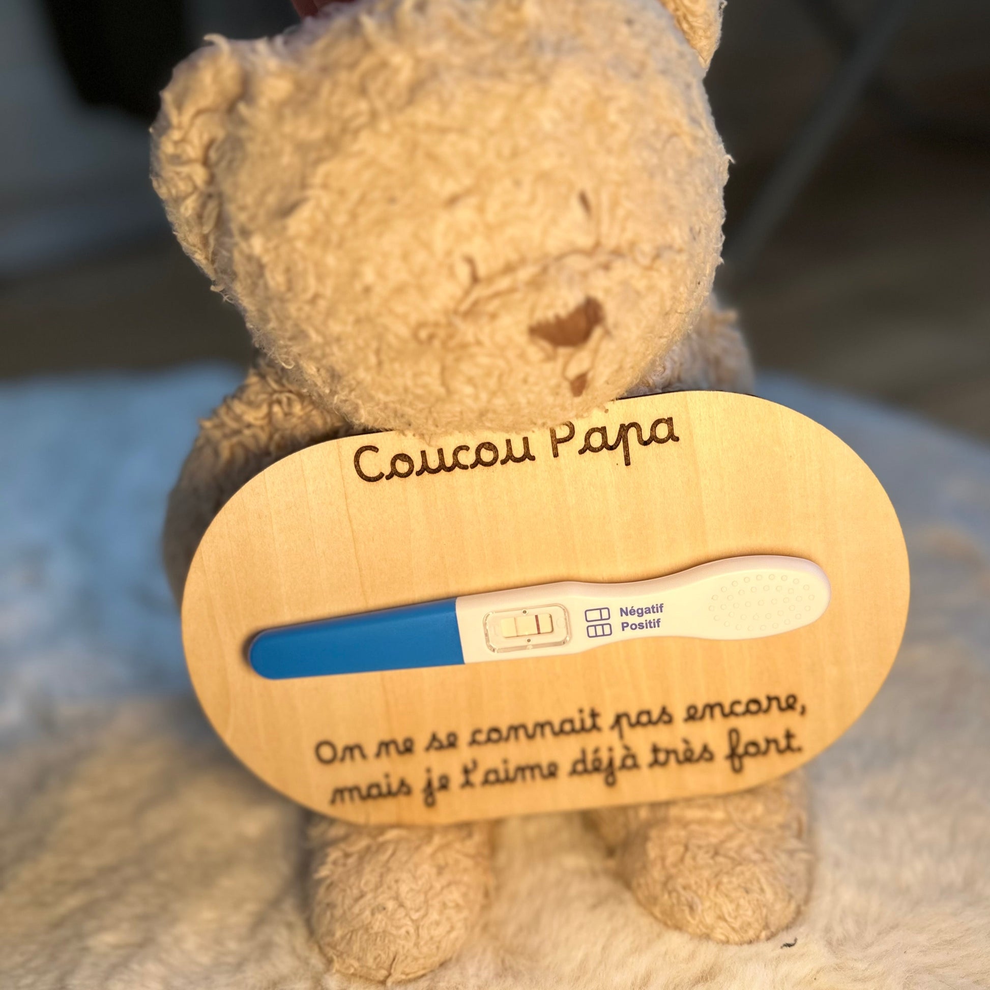 peluche tenant une carte en bois "coucou papa, on ne se connait pas encore, mais je t'aime déjà très fort" et un test de grossesse positif