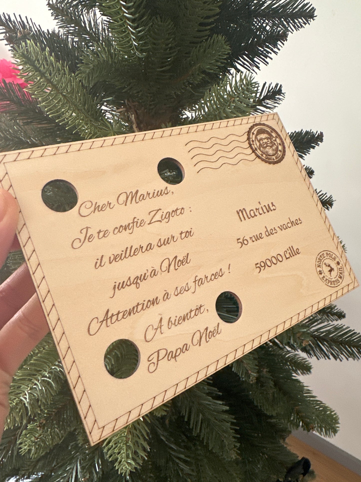 Lettre personnalisée de Papa Noël tenue en main, avec fond lumineux de sapin de Noël en bois