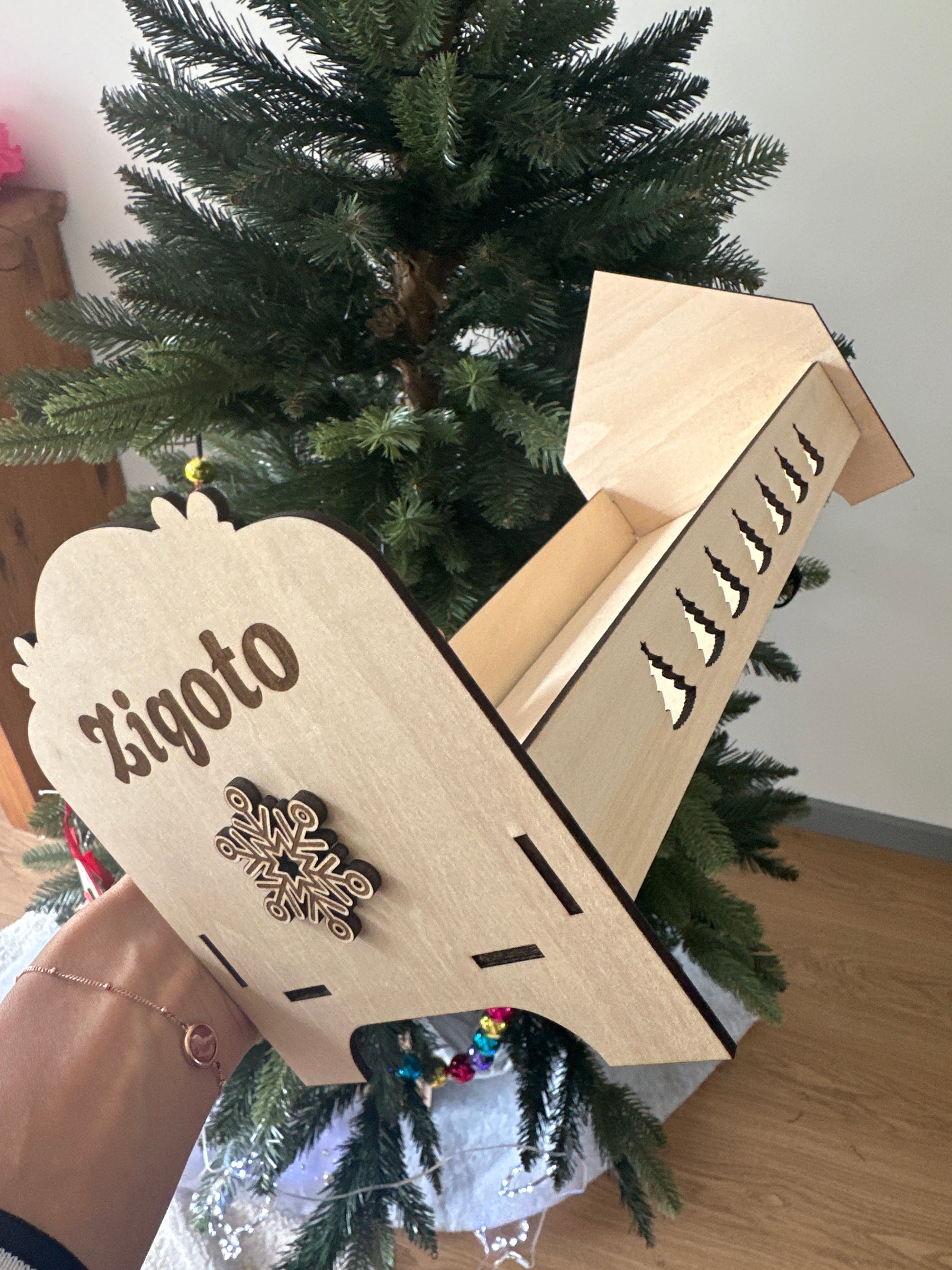 Lit de lutin farceur en bois personnalisé “Zigoto”, décoré d’un flocon, posé au pied d’un sapin de Noël.