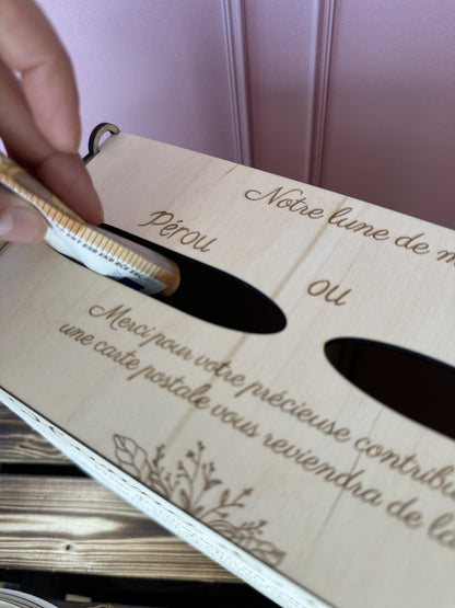 une main glisse des billets dans l'encoche "Pérou" de l'urne mariage en bois