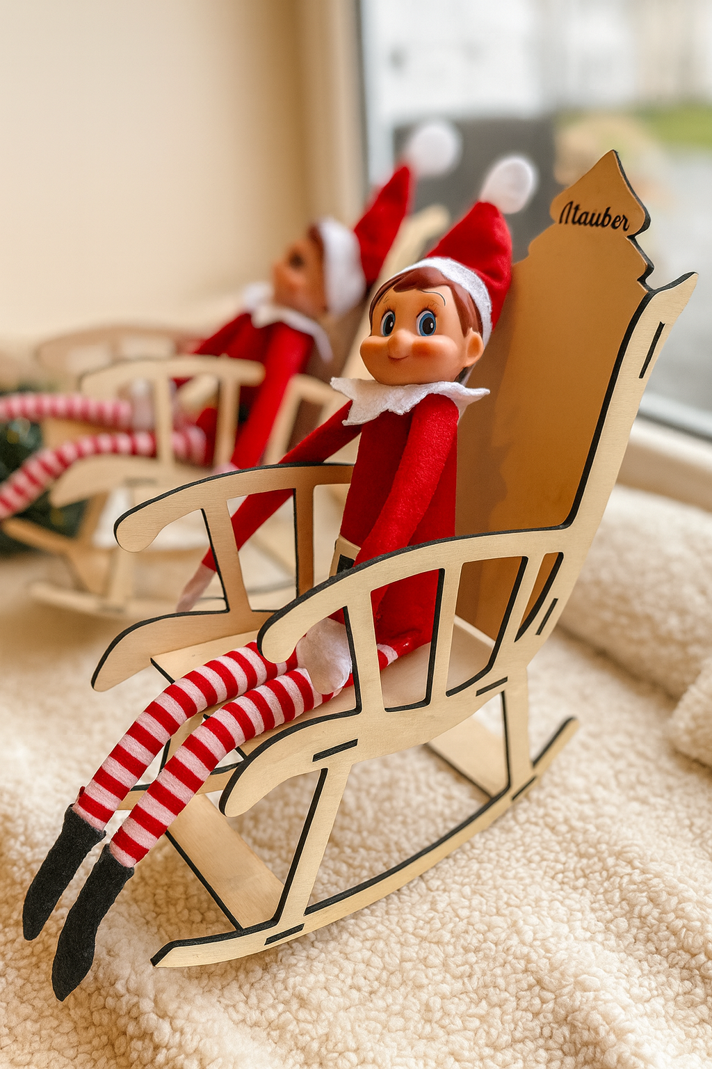 Deux lutins farceurs assis dans leurs rocking chairs en bois, placés l’un derrière l’autre près d’une fenêtre. Le lutin au premier plan est net tandis que l’arrière-plan est flou, mettant en valeur les chaises artisanales