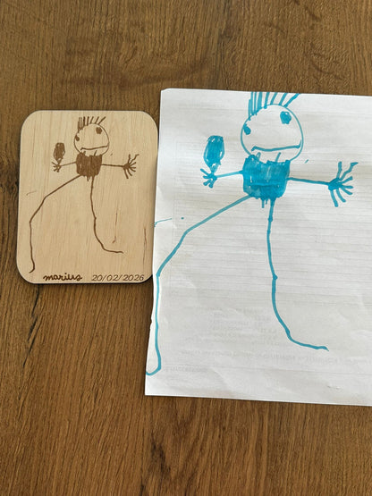 un dessin d'un bonhomme réalisé par un jeune enfant placé à côté du même dessin reproduit sur une carte en bois et signé "marius 20/02/2026"