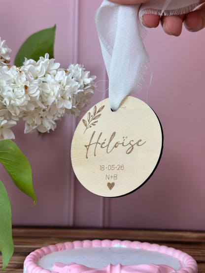 un marque place en bois personnalisé avec le prénom de l'invité gravé, la date du mariage, les initiales des mariés et des motifs végétaux. suspendu par un ruban en satin pour un souvenir du mariage