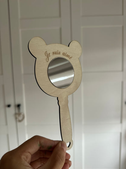 Miroir mantra en bois forme ours, gravé "je suis aimé", prénom personnalisé, création artisanale Chou Rose fait main. tenu par une main en face d'un placard
