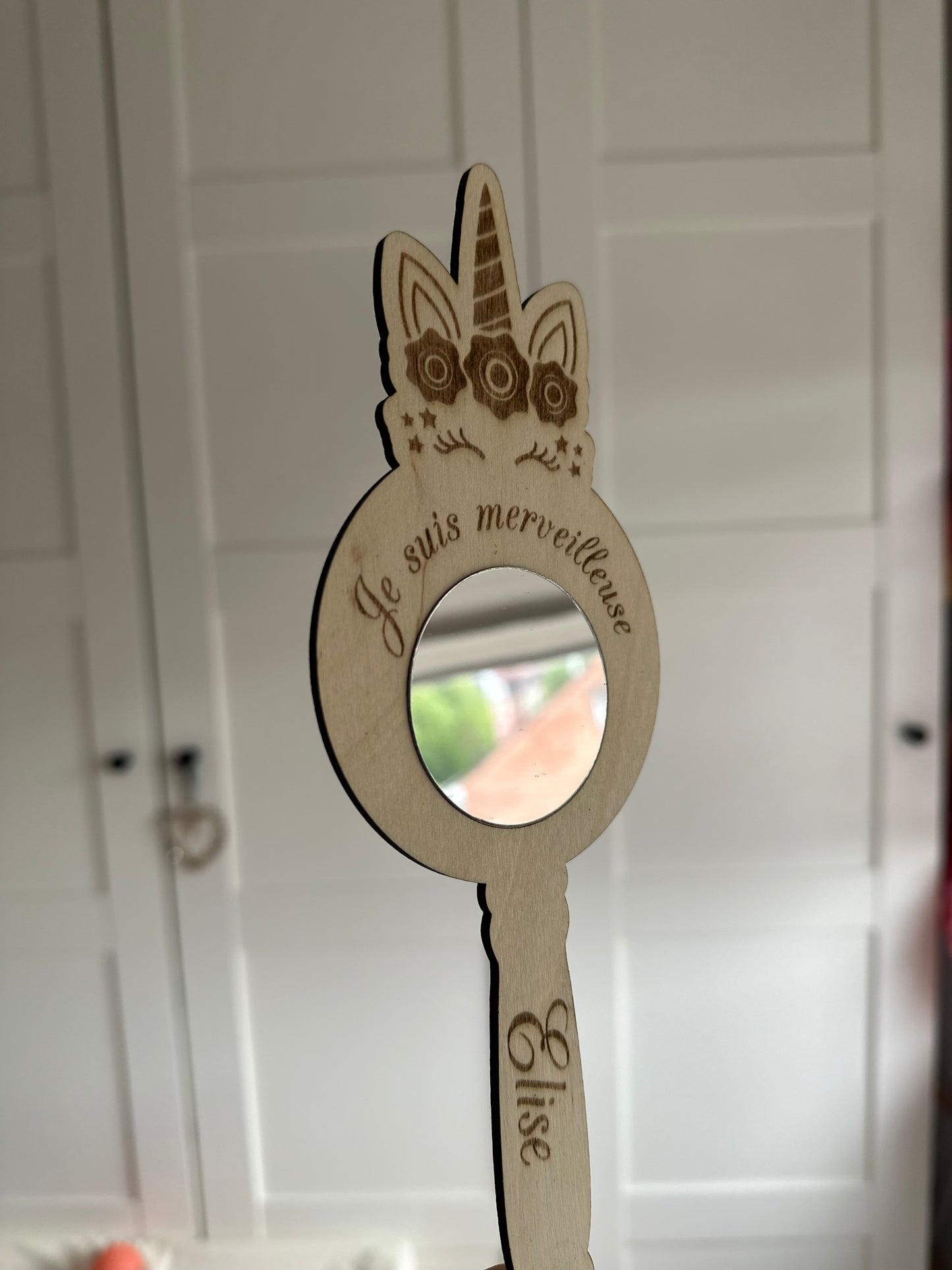 miroir mantra en forme de licorne en bois gravé "je suis merveilleuse" et "Elise" tenu devant un placard blanc