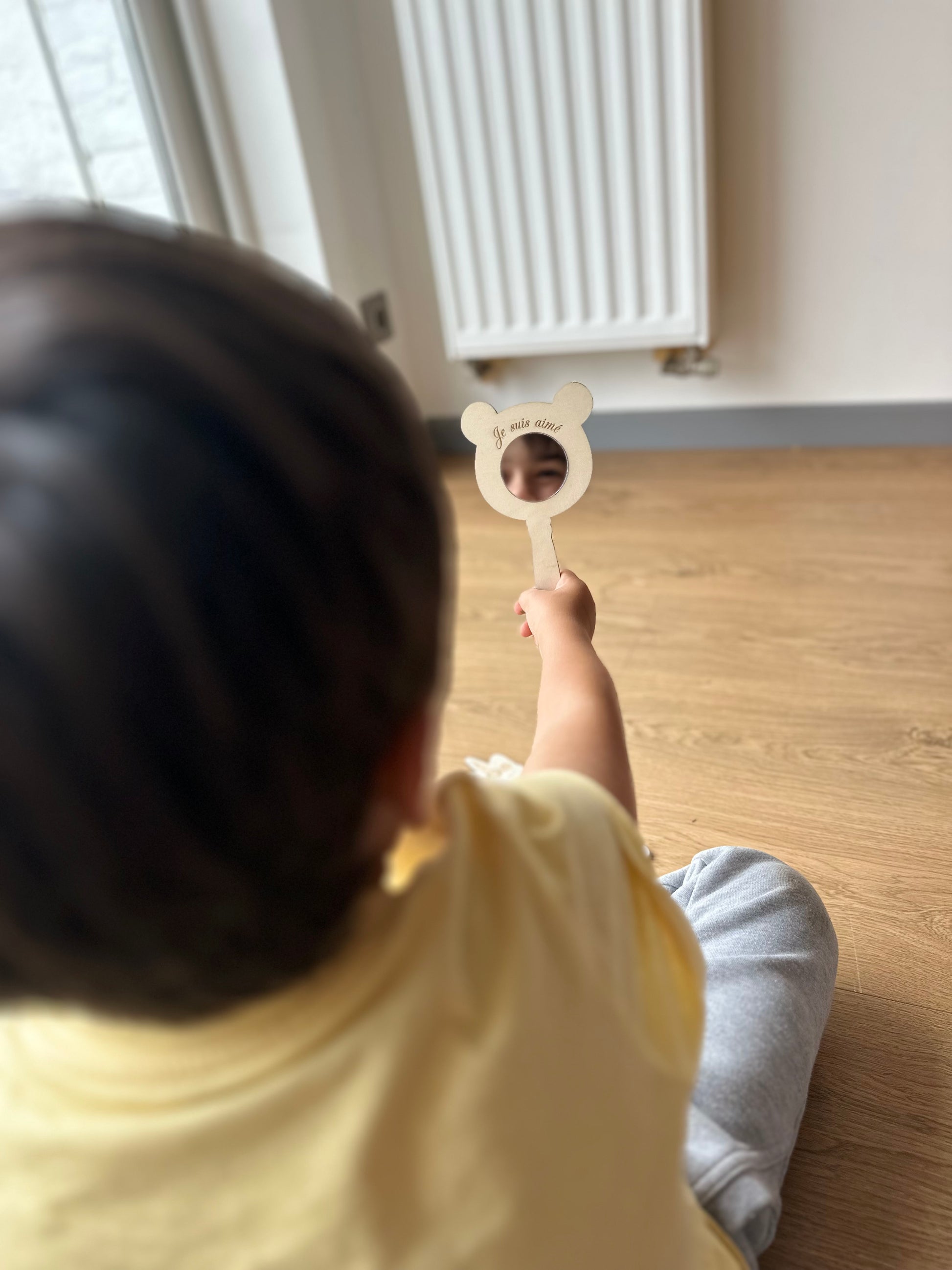 petit garçon de dos se regarde dans un miroir en forme d'ours où il est gravé "je suis aimé"