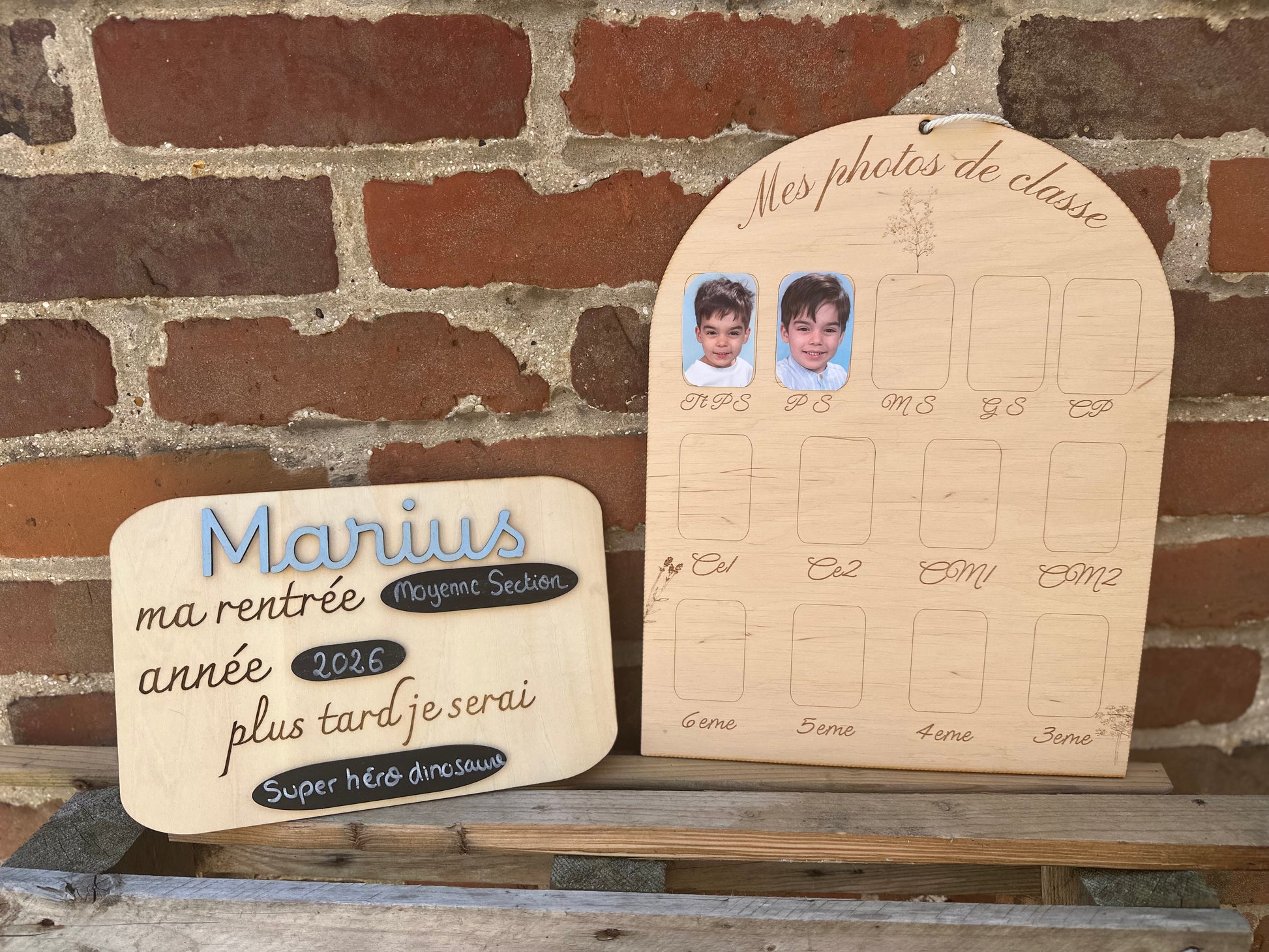 panneau ma rentrée modifiable et pancarte photo personnalisée en bois ; les 2 panneaux sot posés sur une palette en bosi en face d'un mur de briques rouges : le premier "Marius" bleu ma rentrée "moyenne section" année "2026" et plus tard je serai "super héros dinosaure" et sur le panneau photos on voit déjà 2 photos sur les cases TTPS et PS d'un petit garçon sur fond bleu 
