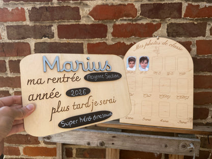 panneau ma rentrée modifiable et pancarte photo personnalisée en bois ; les une main tient le panneau Marius peint en bleu clair, et le  panneau "mES PHOTOS DE CLASSE" est posé sur une palette en bois en face d'un mur de briques rouges : le premier "Marius" bleu ma rentrée "moyenne section" année "2026" et plus tard je serai "super héros dinosaure" et sur le panneau photos on voit déjà 2 photos sur les cases TTPS et PS d'un petit garçon sur fond bleu 
