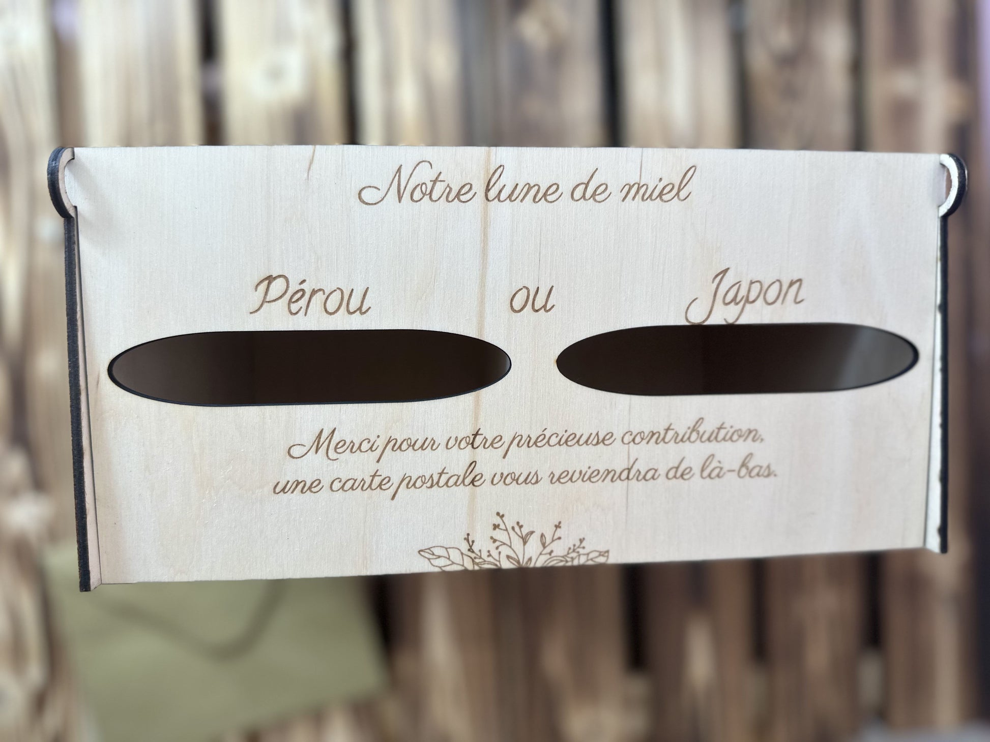 urne en bois mariage personnalisée avec 2 entrées pour les 2 destinations à voter : "Pérou ou Japon" "notre lune de miel" "merci pour votre précieuse contribution, une carte postale vous reviendra de là-bas" l'urne est vue du ciel, posée sur une table palette en boisn on aperçoit une enveloppe posée sur la table