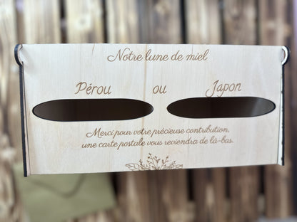 urne en bois mariage personnalisée avec 2 entrées pour les 2 destinations à voter : "Pérou ou Japon" "notre lune de miel" "merci pour votre précieuse contribution, une carte postale vous reviendra de là-bas" l'urne est vue du ciel, posée sur une table palette en boisn on aperçoit une enveloppe posée sur la table