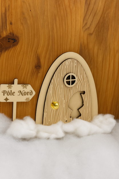 Porte de lutin farceur en bois posée sur un décor de neige artificielle, avec panneau “Pôle Nord” et fond imitation bois.
