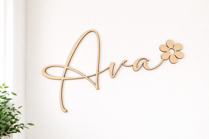 prénom en bois découpé au laser dans une police élégante et moderne : Ava, le prénom se termine par une fleur type marguerite. Le prnéom est fixé sur un mur blanc, à côté d'une fenêtre; IL Y A UNE PLANTE GRASSE SUR LE CÔTÉ