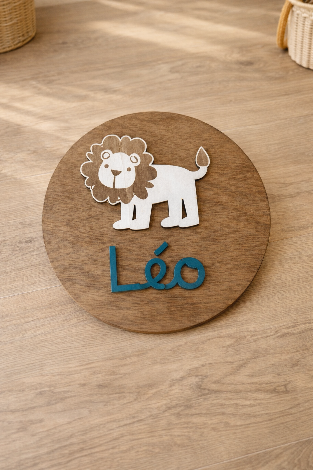 disque en bois personnalisé avec le prénom Léo peint en bleu océan et un lion en bois fixé au dessus pour une décoration de chambre unique. lE DISQUE EST POSÉ SUR UNE COMMODE en bois, prêt de 2 paniers en osier