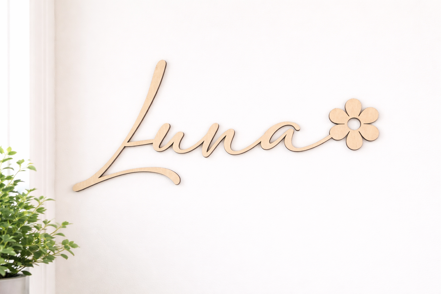 le prénom est découpé au laser : Luna, le prénom se termine par une fleur en bois. Il est fixé sur un mur blanc prêt d'une fenêtre