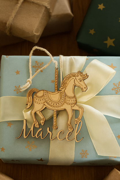 cheval de carrousel en bois personnalisé avec prénom de l'enfant "marcel" et posé sur un cadeau bleu cel avec des étoiles et un ruban blanc